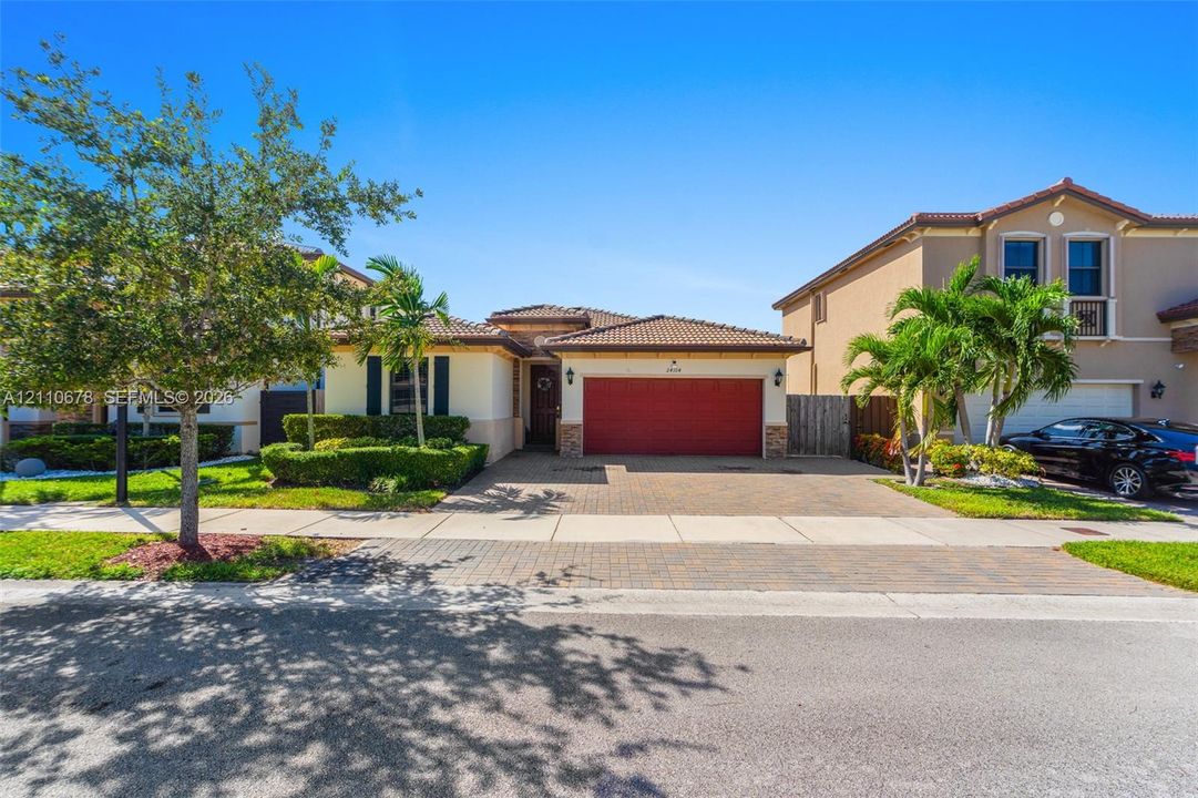 Stucco exterior with a tiled roof, paver driveway, and an attached two-car garage
