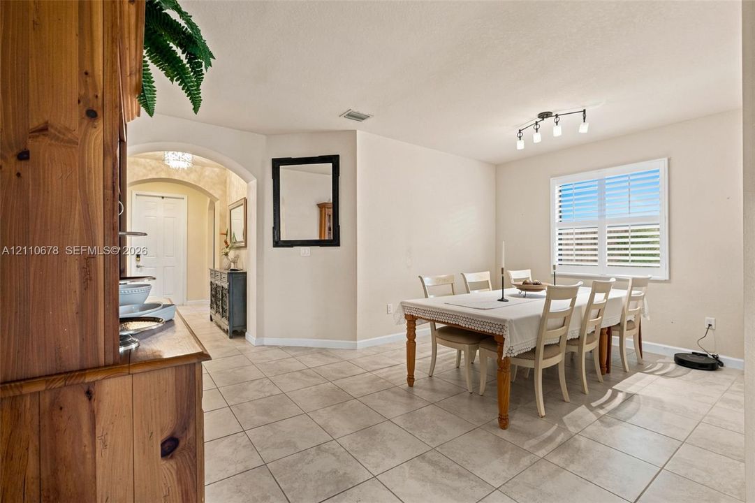 Dining area featuring large-format tile flooring, arched wall detailing, and shuttered window treatments illuminated by multi-light track lighting