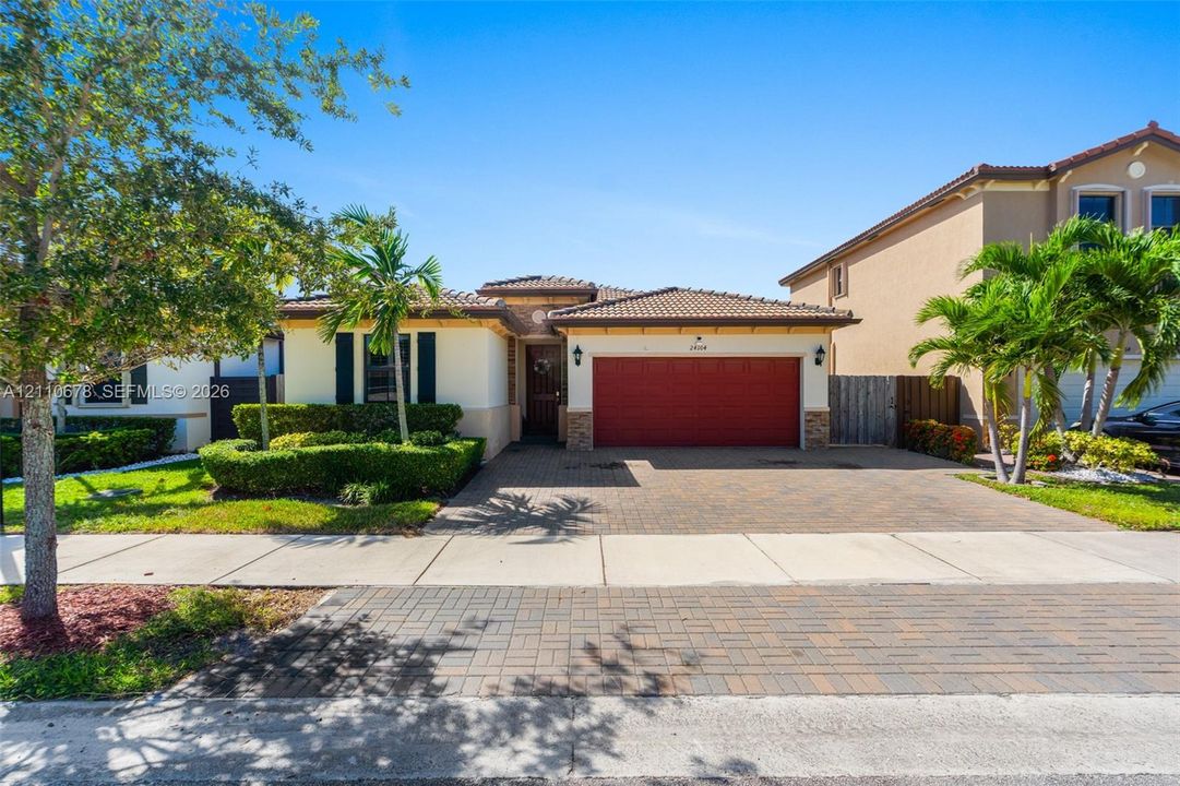 Single-story residence featuring a tiled roof, paver driveway, two-car garage, stone facade accents, and manicured landscaping
