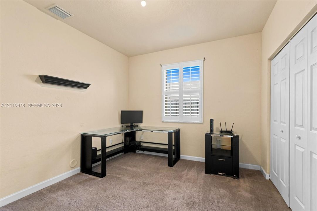 Interior room featuring neutral wall tones, wall-to-wall carpeting, a window outfitted with white plantation-style shutters, and a built-in double-panel closet