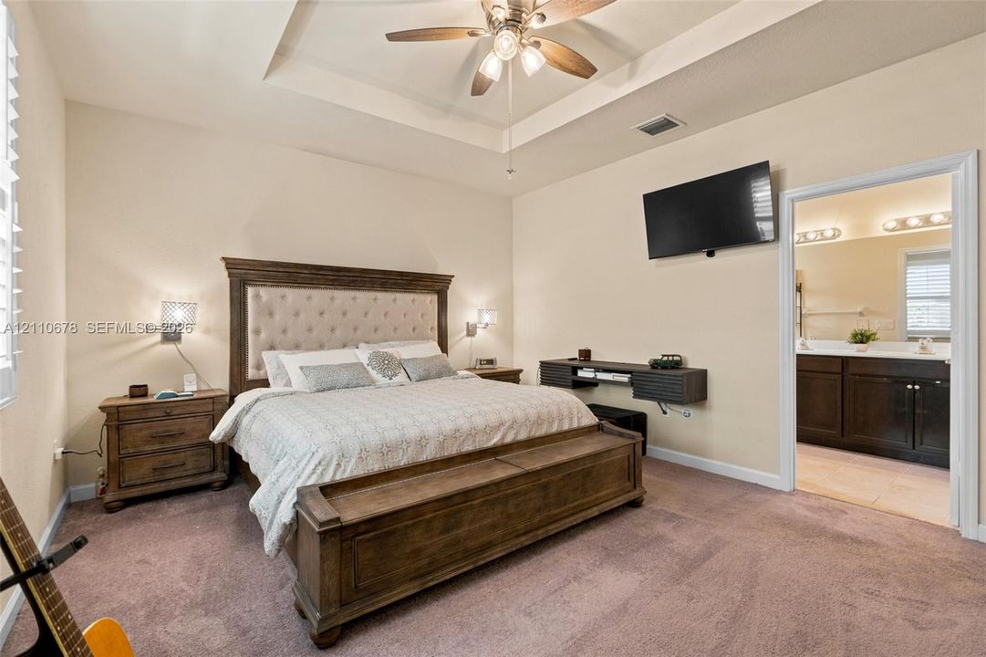 Tray ceiling featuring a center-mounted multi-blade ceiling fan, wall-mounted light fixtures, and carpeted flooring