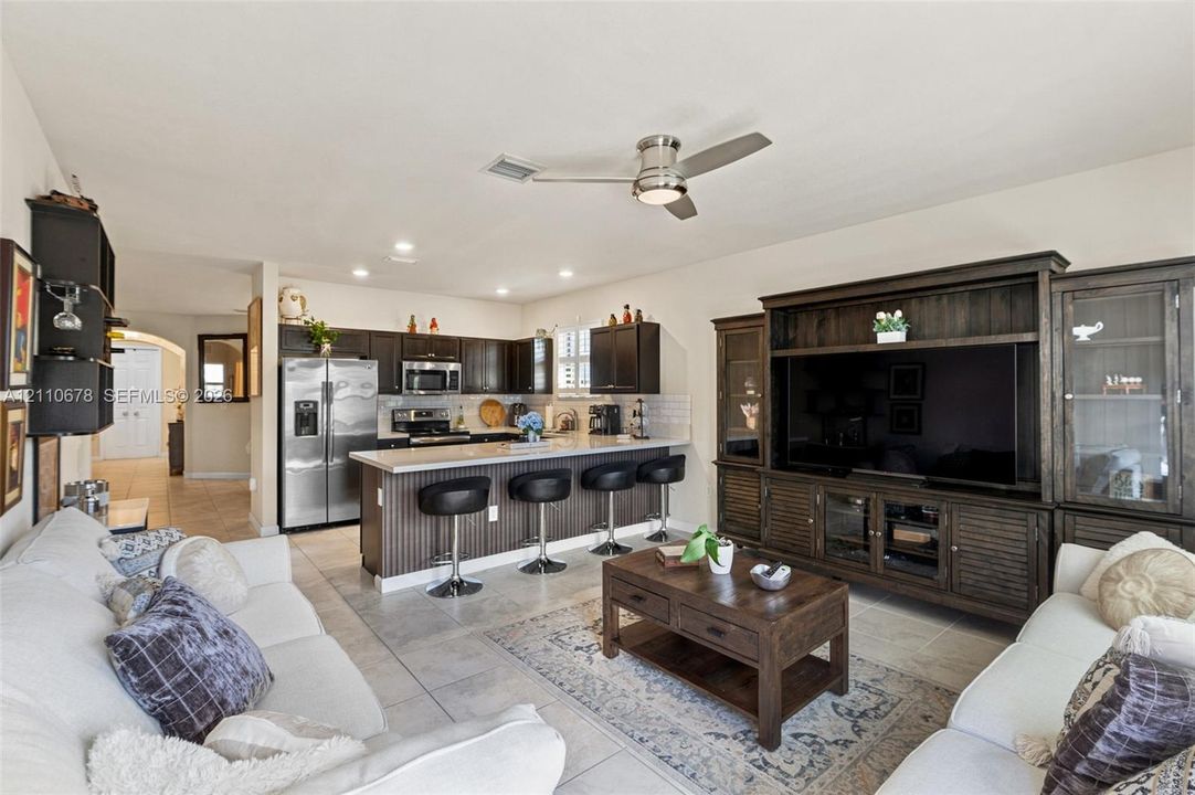 Kitchen featuring dark-finish cabinetry, stainless steel appliances, and a breakfast bar with stone-surface countertop, complemented by ceramic tile flooring and a ceiling-mounted fan