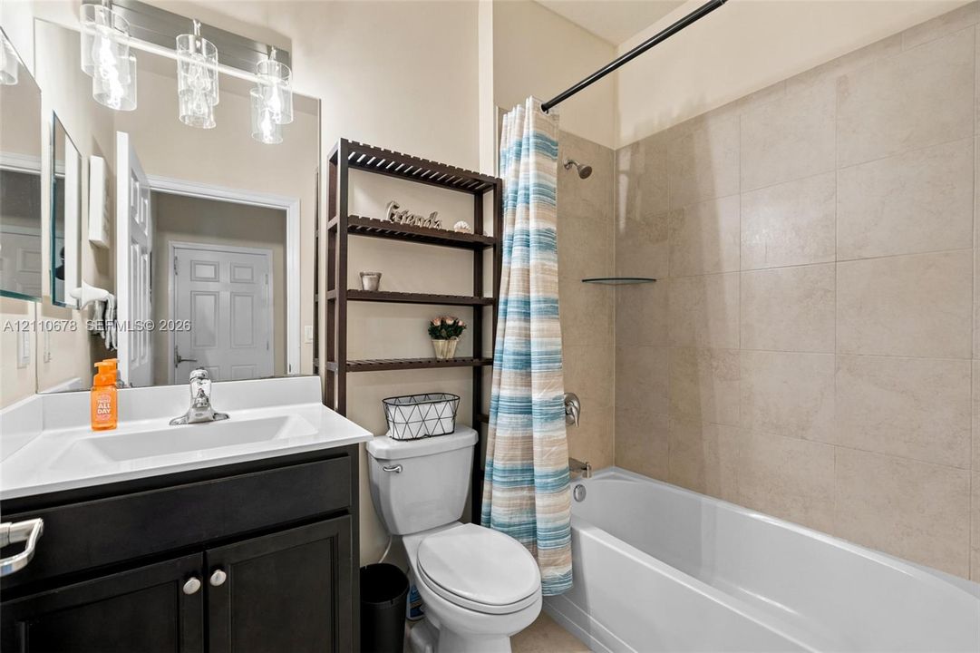 Bathroom featuring a dark-finish vanity with a rectangular sink, large wall-mounted mirror, three-light fixture, and a tub-shower combination with floor-to-ceiling tile surround