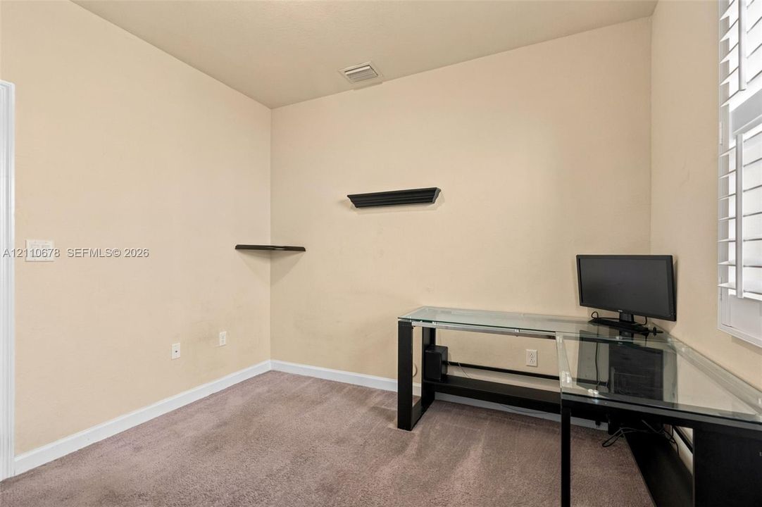 Room featuring neutral wall tones, carpeted flooring, two wall-mounted floating shelves, and white plantation shutters