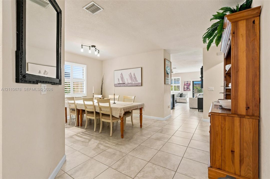 Dining area featuring large-format neutral floor tile, louvered window shutters, and a multi-bulb track lighting fixture