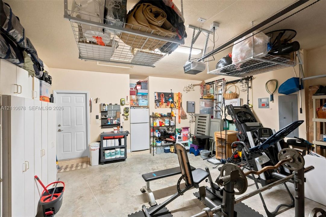 Multi-car garage featuring overhead steel storage racks, white wall-mounted cabinetry, and concrete flooring