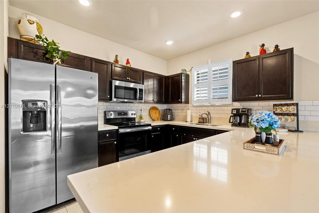 Kitchen featuring dark wood cabinetry, solid surface countertops, stainless steel appliances, subway tile backsplash, and recessed lighting