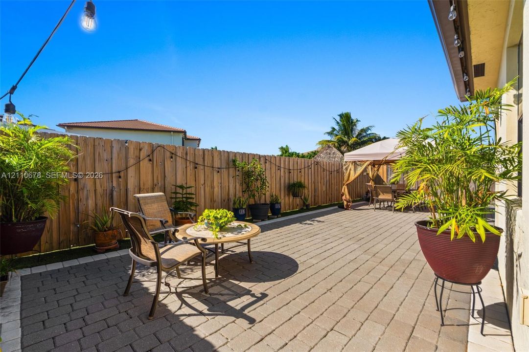 Private rear patio featuring concrete paver flooring, wood-style privacy fencing, and exterior string lighting