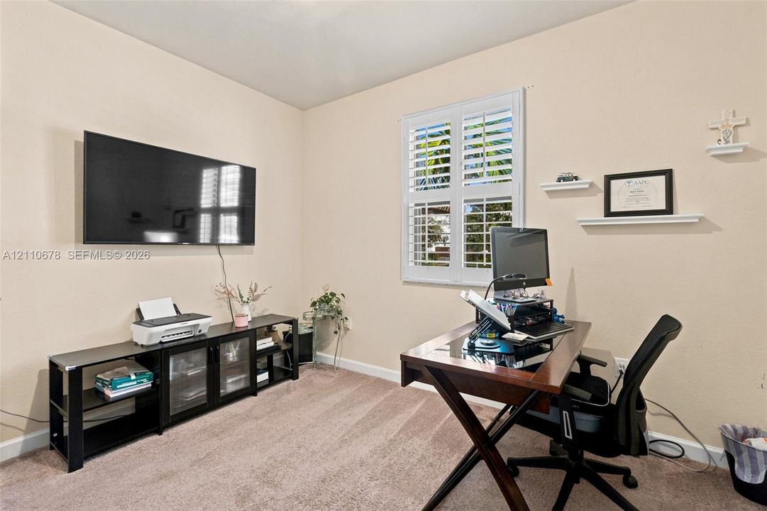 Room featuring neutral wall tones, wall-to-wall carpeting, and a window outfitted with white plantation shutters