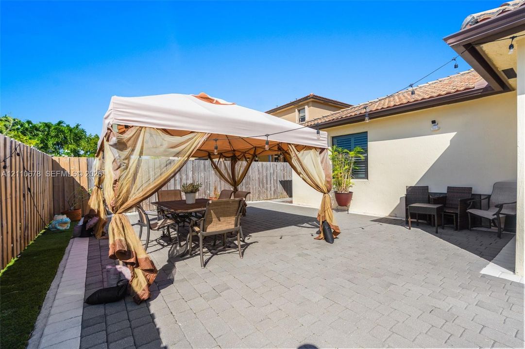Rear patio featuring stone-paver flooring, wood-style privacy fencing, and exterior string lighting