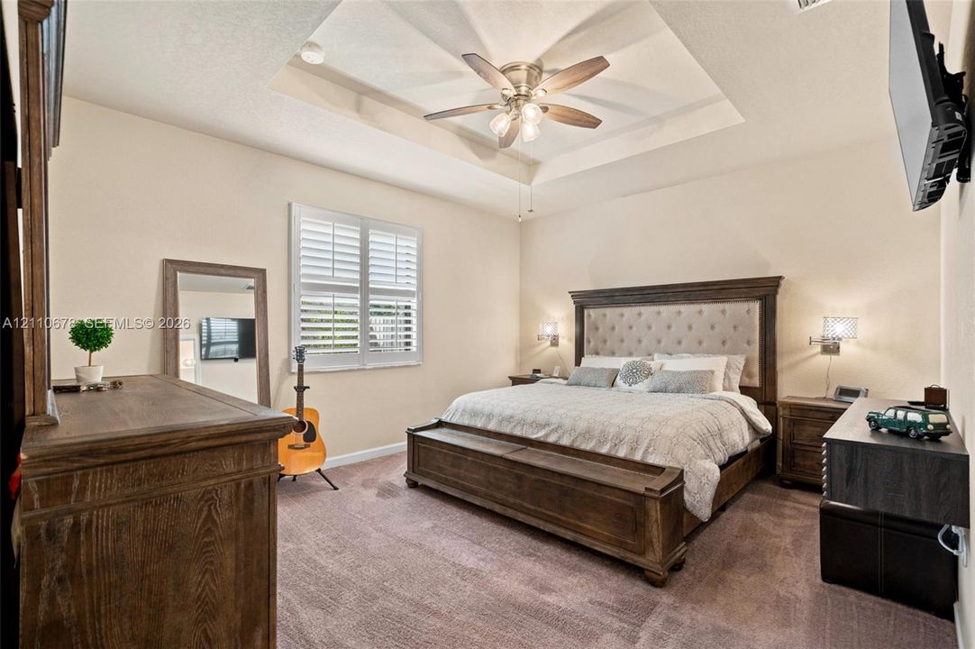 Tray ceiling with a central multi-blade ceiling fan, wall-mounted light fixtures, and window shutters