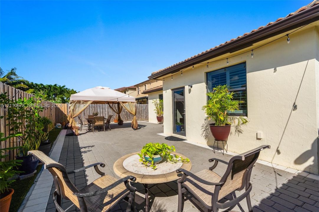 Backyard patio featuring extensive grey paver hardscaping, a tile-bordered edge, and privacy-focused wood fencing