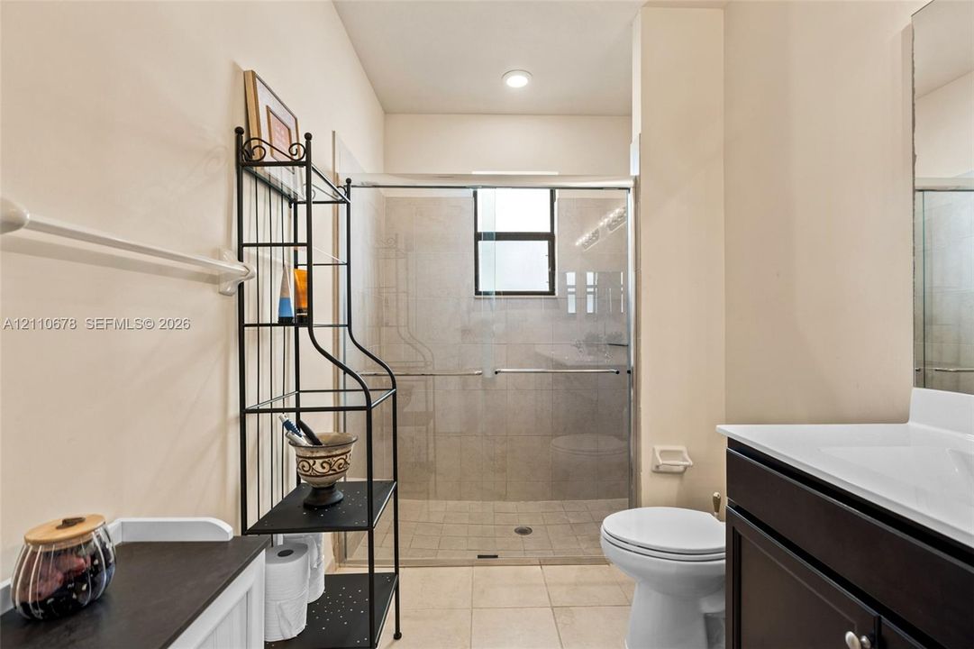 Enclosed shower with sliding glass doors, neutral tile surround, dark-finish vanity cabinet, integrated sink, and recessed lighting