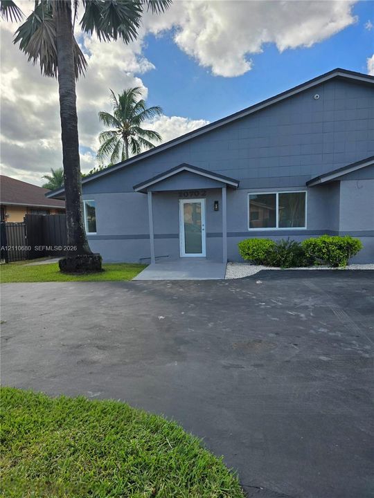 Single-story exterior featuring a gray stucco facade, covered entryway, and asphalt driveway