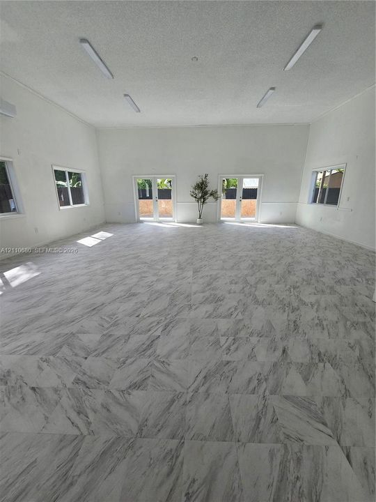 Expansive interior space featuring stone-finish tile flooring, high ceilings with linear lighting, dual glass-paneled double doors, and multiple windows