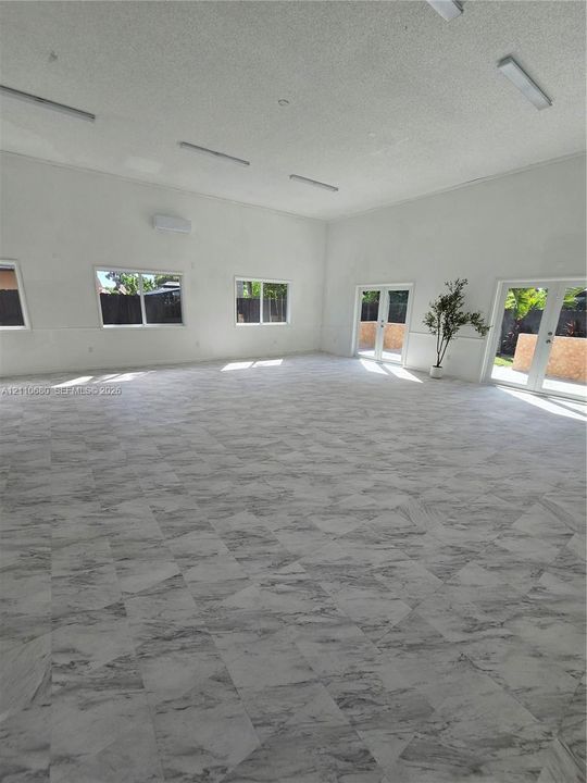 Expansive interior featuring large-format tile flooring, high ceilings, multiple windows, and two sets of double glass doors