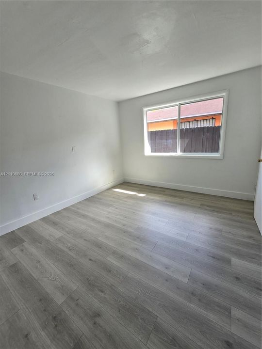 Room featuring light-toned wood-finish flooring, white walls, and a large single-pane sliding window