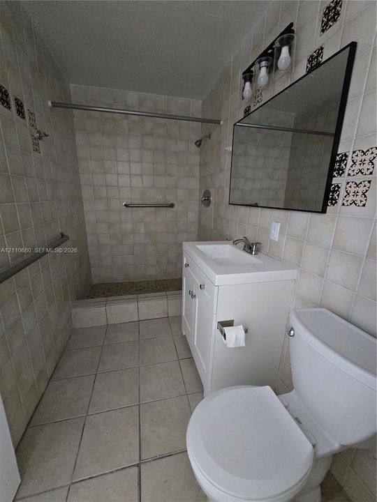 Full bathroom featuring wall-to-wall ceramic tile, a step-in shower stall, white pedestal vanity, and a framed mirror