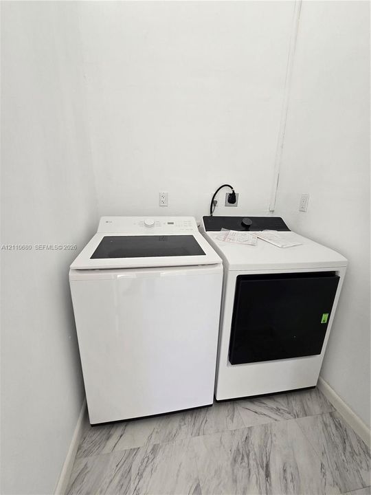 Laundry area featuring large-capacity top-load washer, front-load electric dryer, and light-toned stone-finish tile flooring