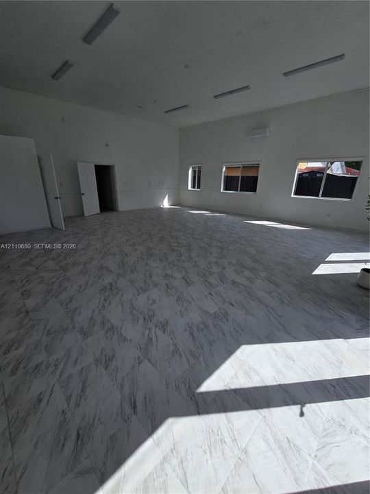 Expansive interior featuring stone-finish tile flooring, recessed linear lighting, wall-mounted climate control unit, and multiple windows