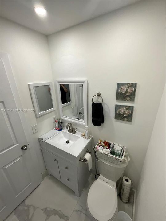 Bathroom featuring a white vanity cabinet with a stone-top integrated sink, a single-handle faucet, a framed mirror, and tile flooring with a neutral-toned vein pattern
