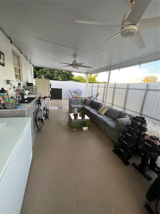 Covered concrete patio featuring two ceiling fans and a built-in stone-finish counter with integrated sink