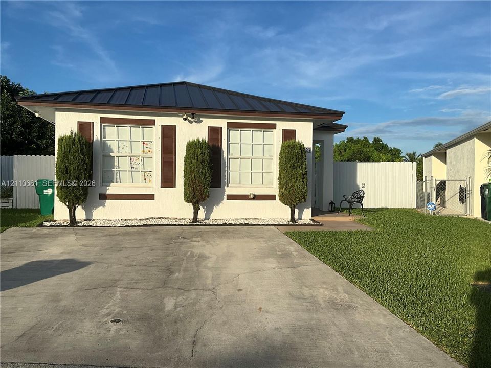 Single-story exterior featuring a metal roof, stucco facade, decorative shutters, and a concrete driveway