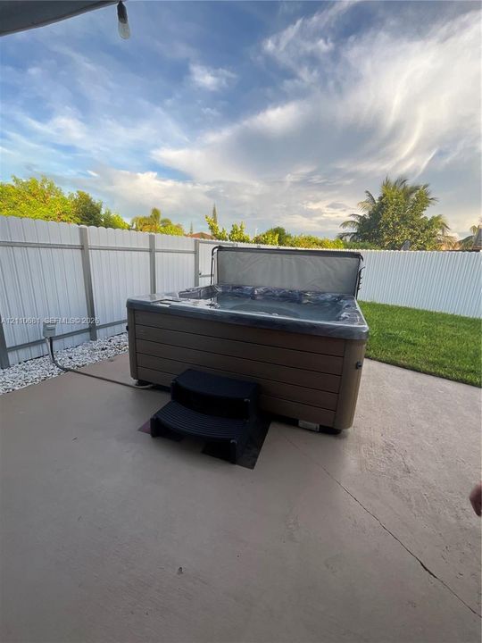Outdoor spa with wood-finish siding, concrete patio, and white vinyl privacy fencing