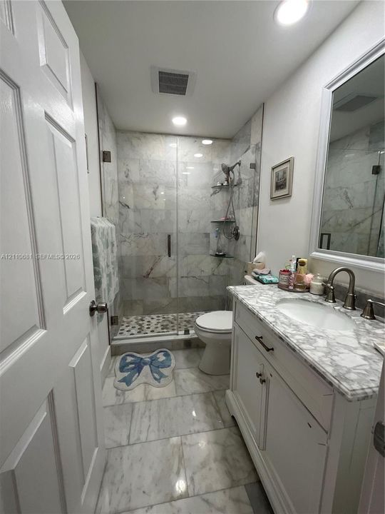 Bathroom featuring a stone-topped vanity with an undermount sink, walk-in shower with a glass enclosure, stone-tiled flooring, and recessed lighting