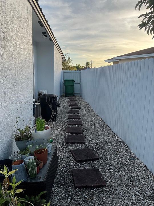 Side yard featuring a white privacy fence, stone ground cover, and square concrete pavers leading to a gated entry