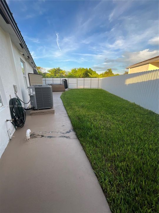 Rear yard featuring a concrete patio, green lawn, and full-perimeter vinyl privacy fencing