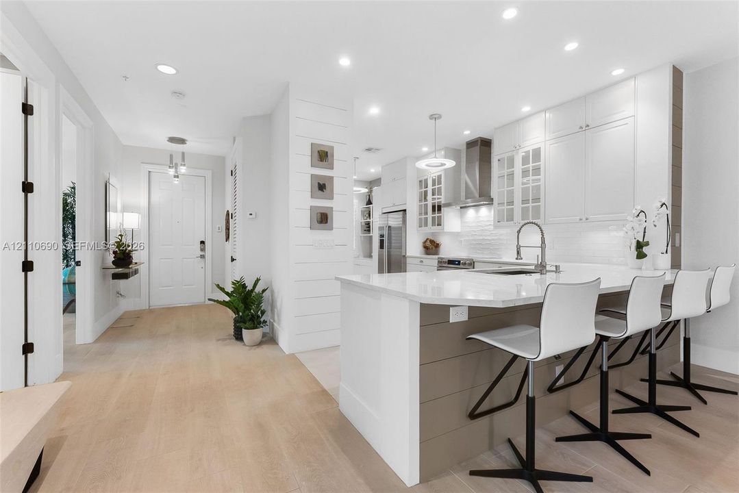 Kitchen featuring a quartz-topped island, white cabinetry with glass-panel accents, stainless steel appliances, shiplap detailing, and wood-finish flooring