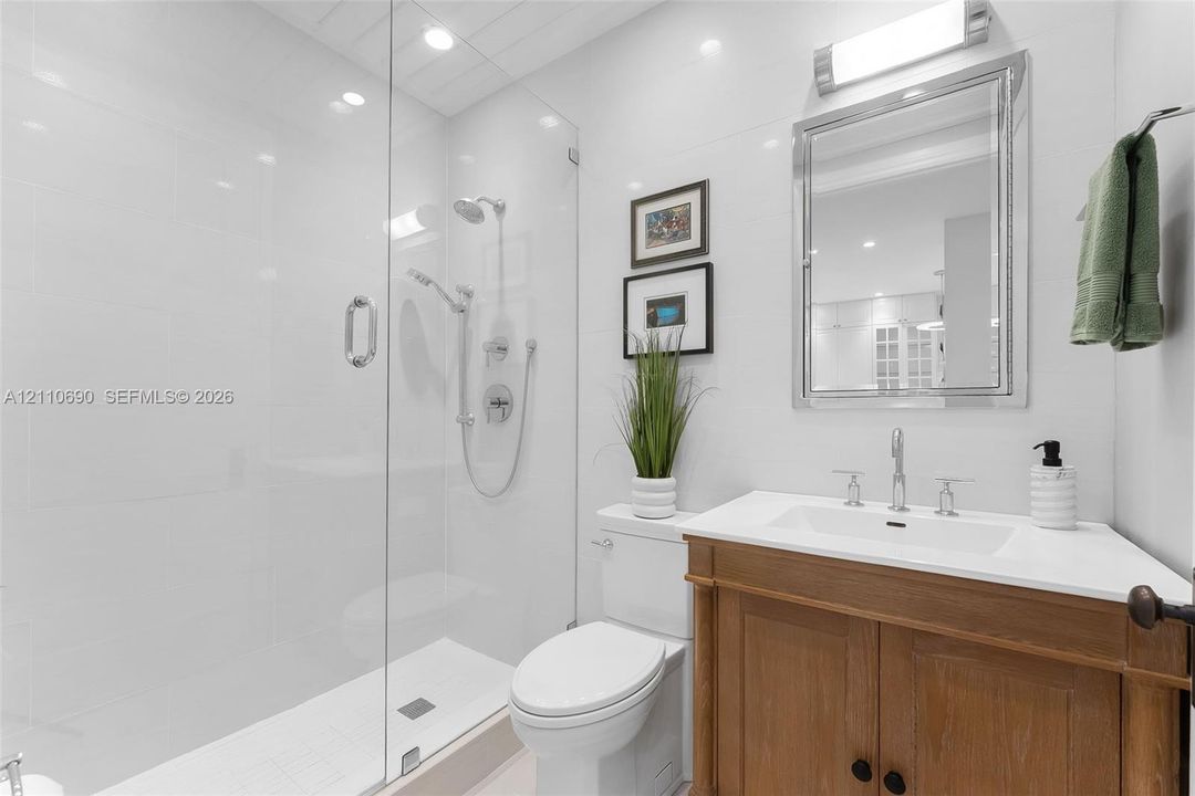 Bathroom featuring a walk-in shower with frameless glass enclosure, handheld shower fixture, wood-finish vanity with countertop sink, and wall-mounted vanity mirror