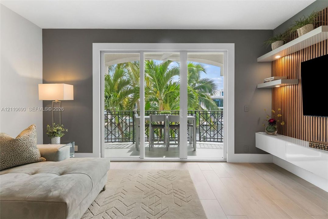 Sliding glass doors opening to a covered balcony with decorative metal railing, wood-slat accent wall with integrated shelving, and white high-gloss floating cabinetry