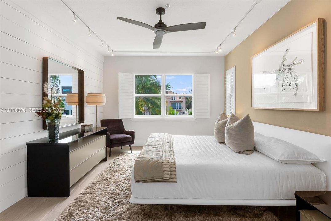 Room featuring horizontal shiplap wall paneling, ceiling-mounted track lighting, a matte finish ceiling fan, and window-mounted interior shutters
