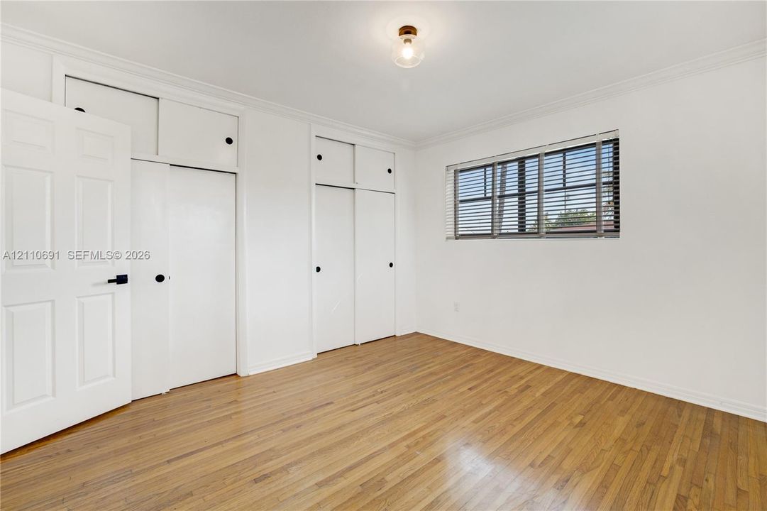 Room featuring wood-finish flooring, white walls, crown molding, multi-panel doors, and built-in floor-to-ceiling cabinetry