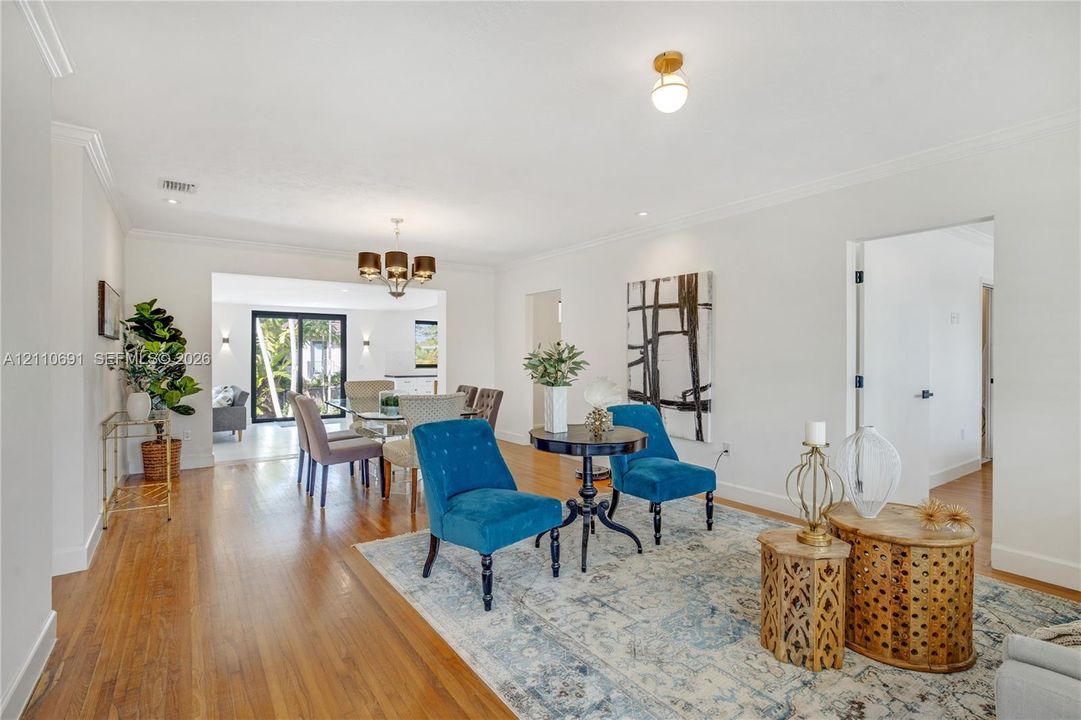 Open-concept interior featuring wood-finish flooring, crown molding, multi-arm chandelier lighting, and sliding glass doors