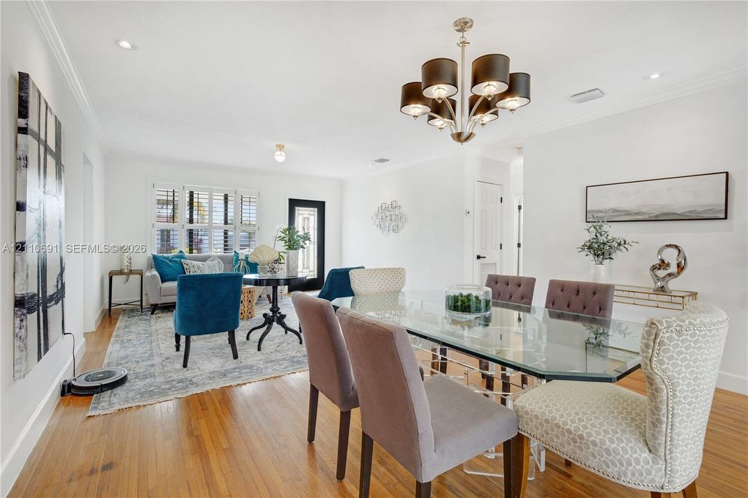 Open-concept interior featuring wood-finish flooring, multi-light chandelier, crown molding, recessed lighting, and multi-pane window with shutter accents