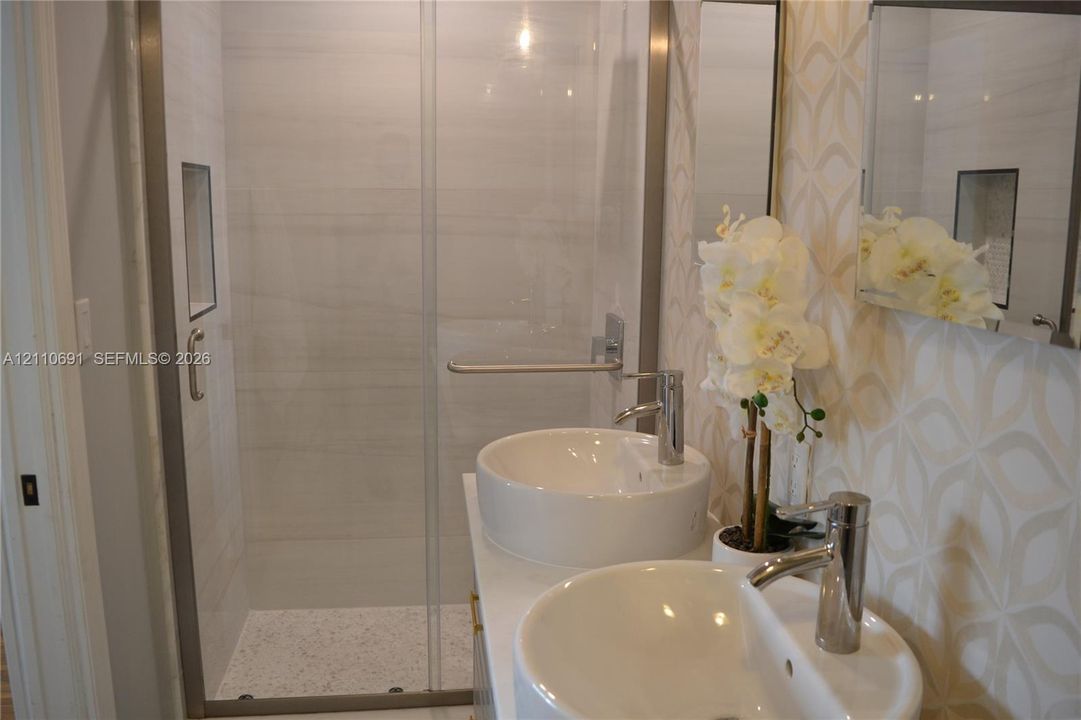 Walk-in shower with horizontal tile surround and integrated wall niche, featuring a dual-sink vanity with circular vessel sinks, polished chrome faucets, and patterned wall tile