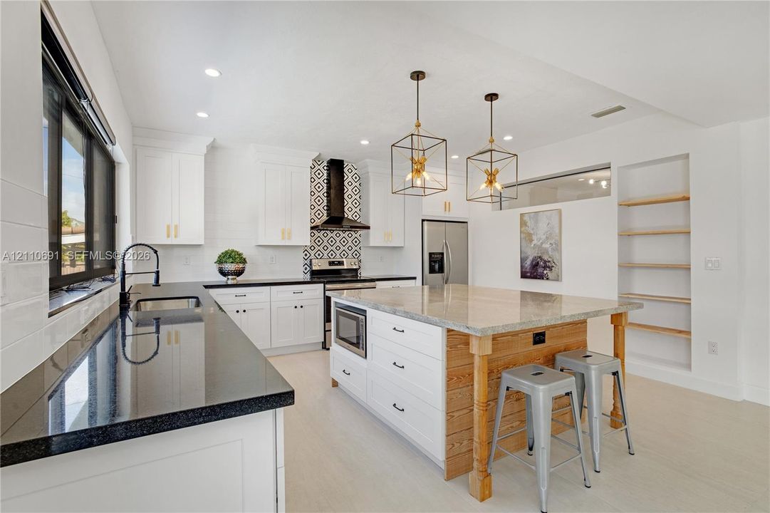 Kitchen featuring white shaker cabinetry, black stone countertops, geometric tile backsplash, central island with wood paneling, and open built-in shelving