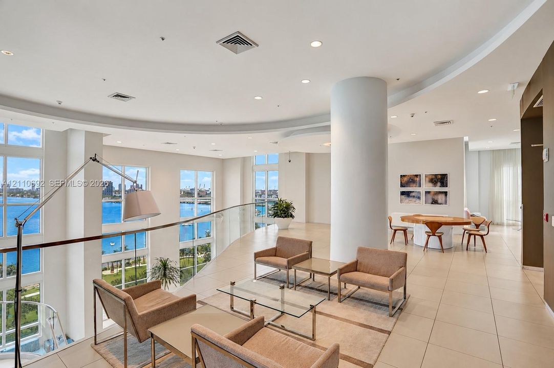 Open floor plan featuring tile flooring, recessed lighting, a curved glass balcony railing, and floor-to-ceiling windows with water scenery