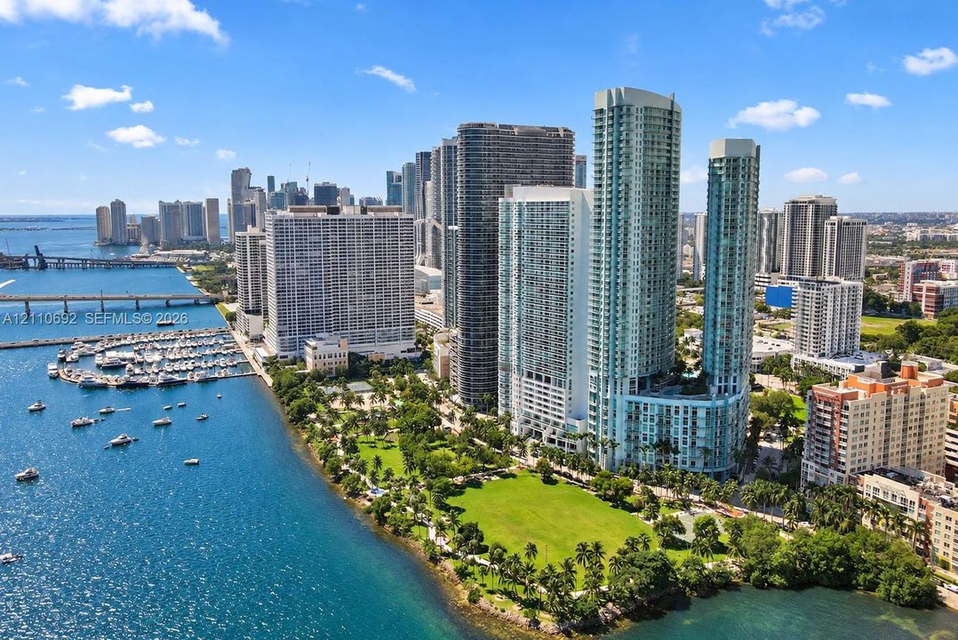 Aerial perspective of high-rise towers featuring glass-paneled facades, waterfront positioning, and proximity to an expansive green space and marina