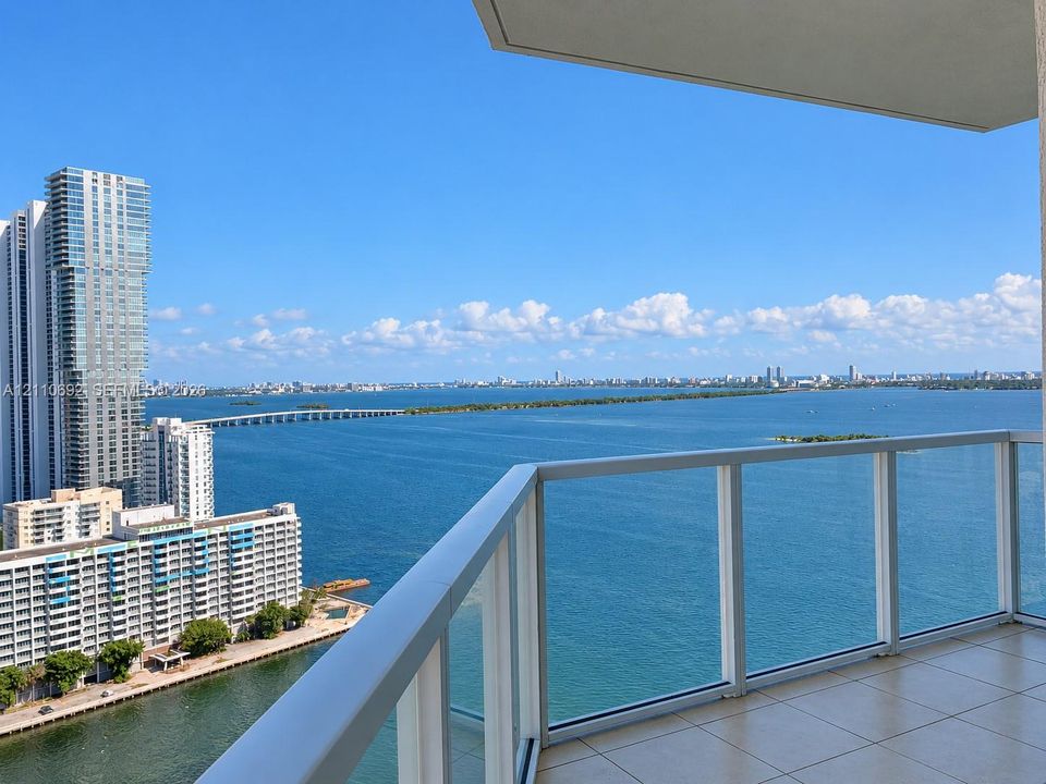 Private balcony featuring glass panel railings and tile flooring, offering expansive water and cityscape scenery