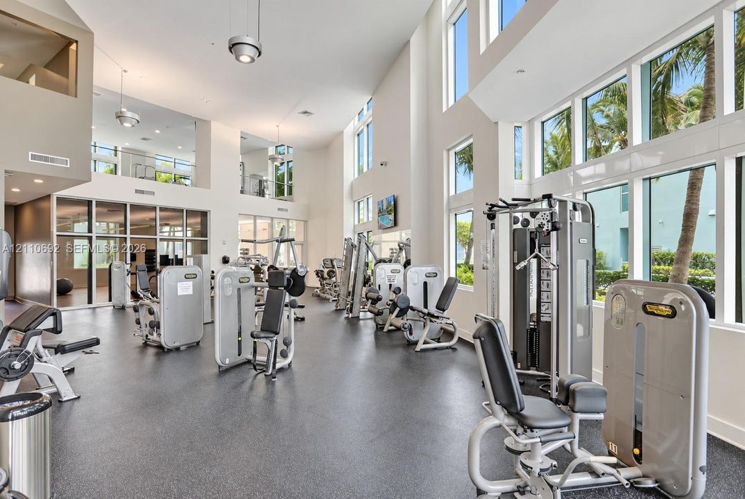 Fitness center featuring double-height ceilings, floor-to-ceiling windows, recessed lighting, and industrial-grade rubber flooring
