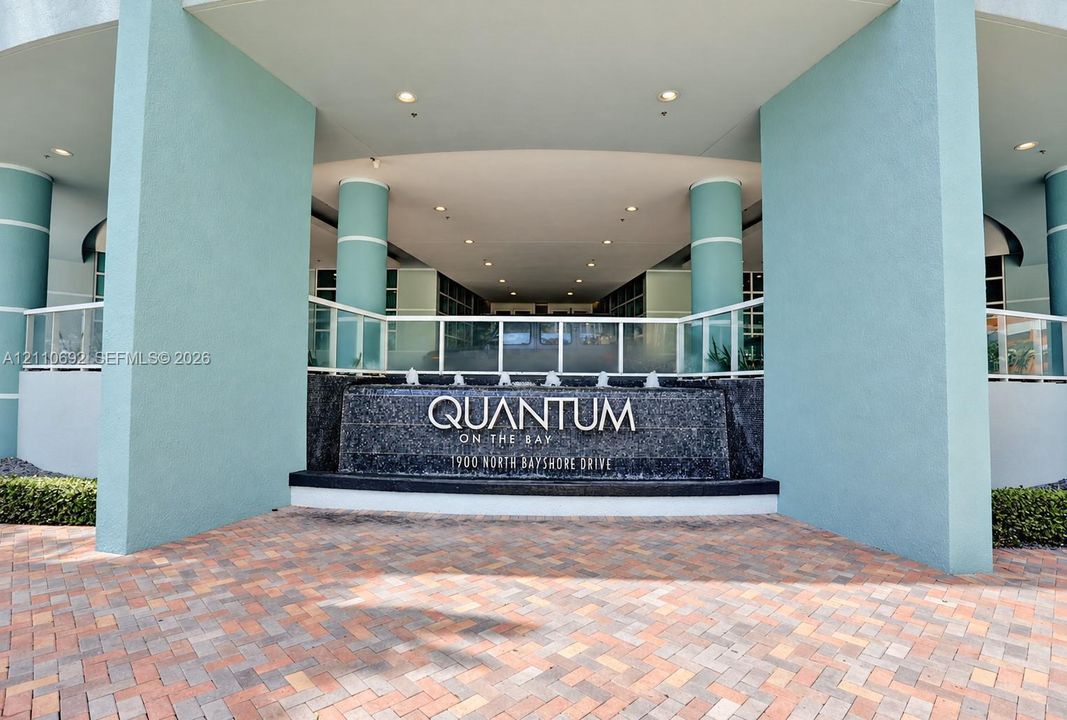 Building entrance featuring a textured stone water feature, patterned brick pavers, recessed ceiling lighting, and structural columns