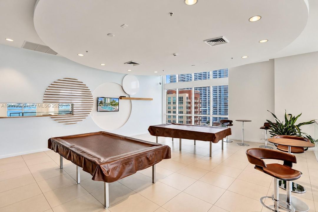 Recreation space featuring large-format tile flooring, a circular dropped ceiling with recessed lighting, floor-to-ceiling windows, and decorative wall-mounted architectural elements