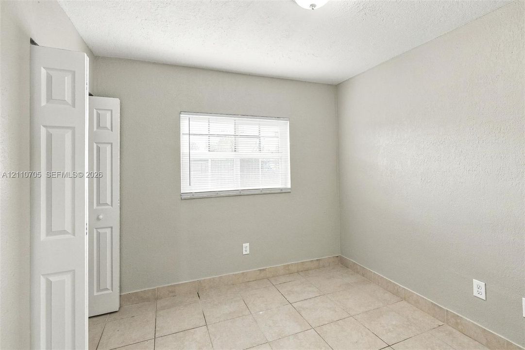 Neutral-toned interior space featuring tile flooring, a recessed window, and bi-fold closet doors