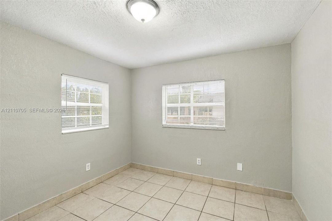 Neutral-toned interior space featuring ceramic tile flooring, dual windows with integrated blinds, and a centered dome ceiling light fixture
