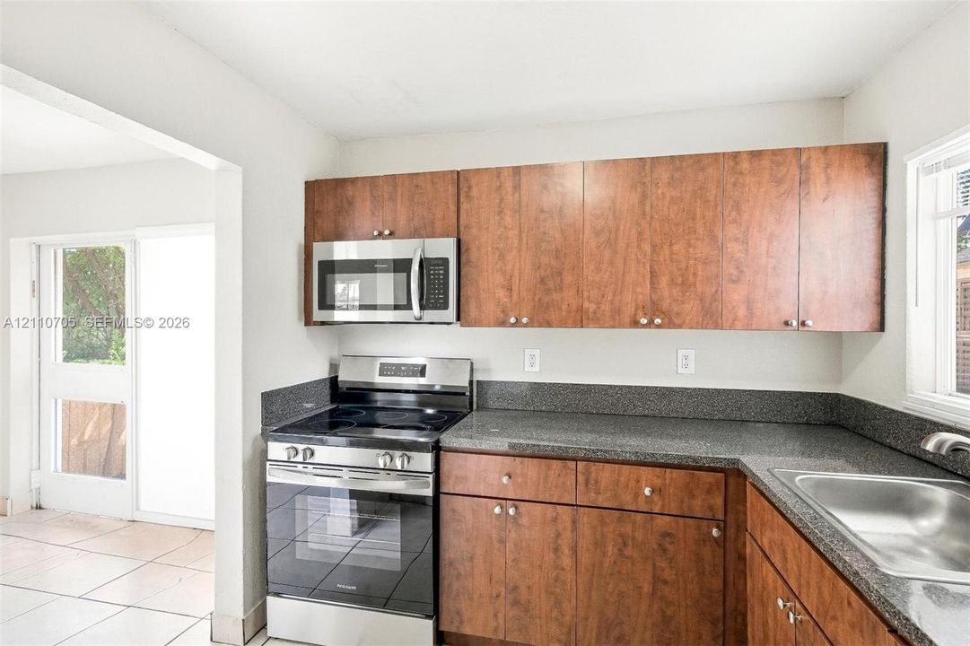Kitchen featuring stained wood cabinetry, stone-finish countertops, stainless steel microwave, and freestanding electric range