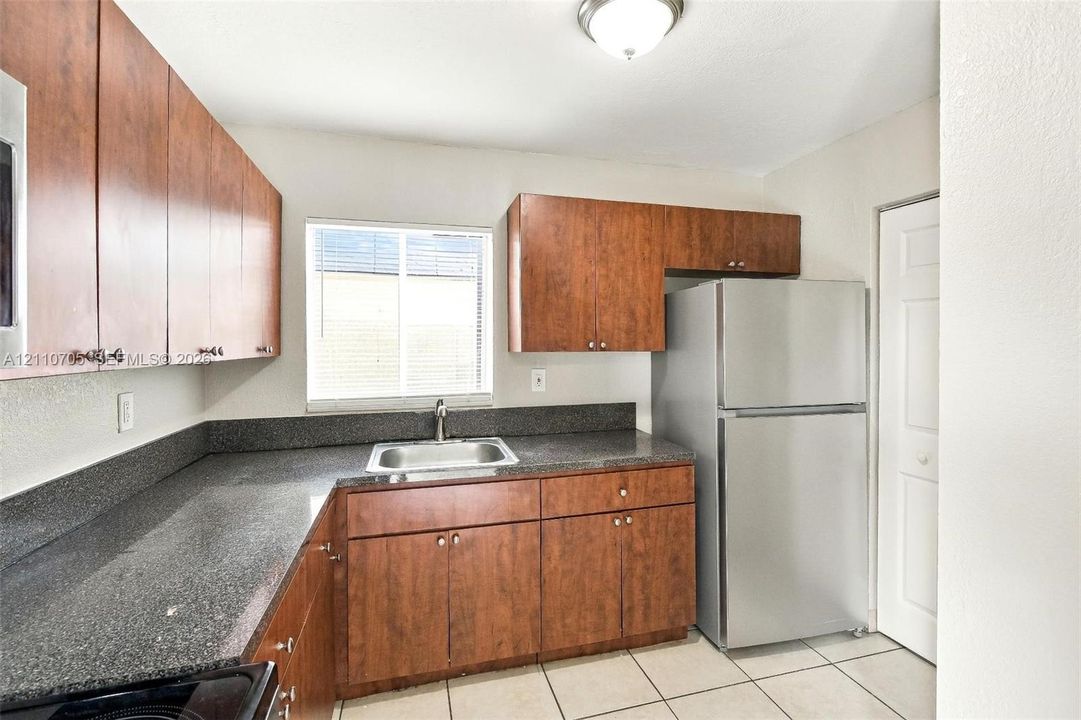 Kitchen featuring wood-finish cabinetry, dark stone-finish countertops, stainless steel refrigerator, undermount sink, and tiled flooring